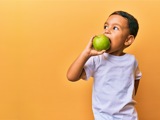A banner with a yellow background, featuring a young boy in a white shirt, eating a green apple